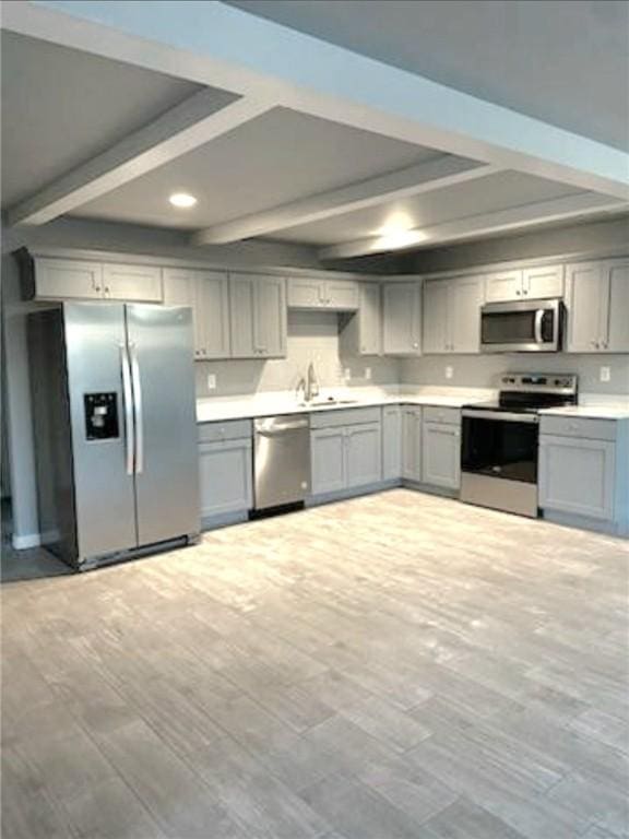 kitchen featuring beam ceiling, light countertops, gray cabinetry, appliances with stainless steel finishes, and a sink