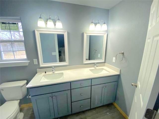 bathroom featuring double vanity, baseboards, toilet, and a sink