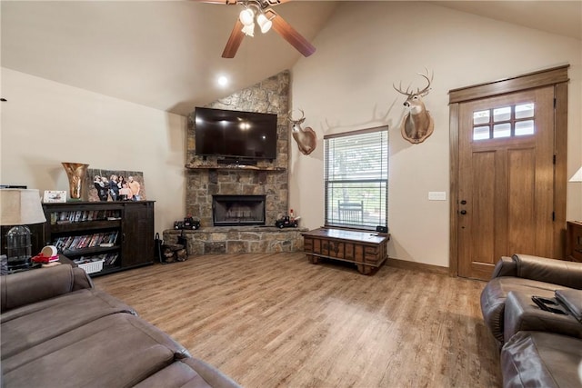 living area featuring ceiling fan, high vaulted ceiling, a stone fireplace, baseboards, and light wood-type flooring