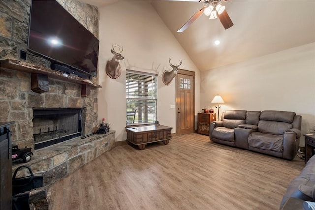 living room with baseboards, ceiling fan, wood finished floors, a stone fireplace, and high vaulted ceiling