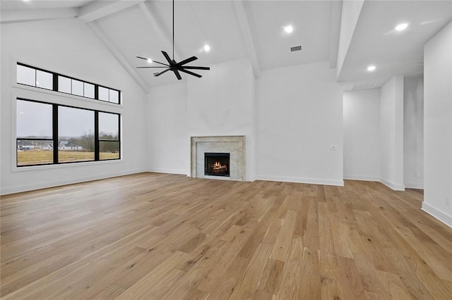 unfurnished living room with beam ceiling, light wood-style flooring, high vaulted ceiling, a lit fireplace, and baseboards