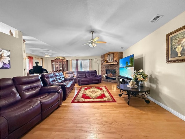 living room featuring visible vents, a ceiling fan, wood finished floors, vaulted ceiling, and a fireplace