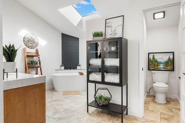 bathroom featuring a skylight, a freestanding bath, toilet, vanity, and baseboards