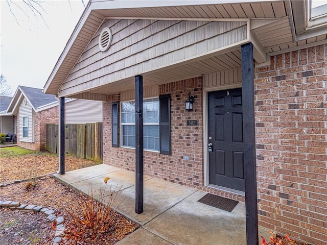 view of exterior entry featuring fence and brick siding