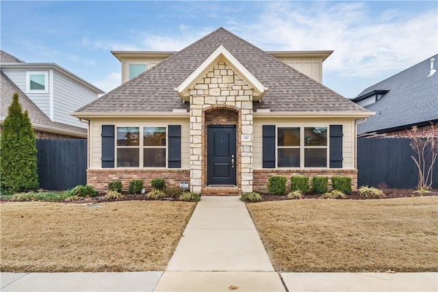 view of front of property with a shingled roof, fence, a front lawn, and brick siding