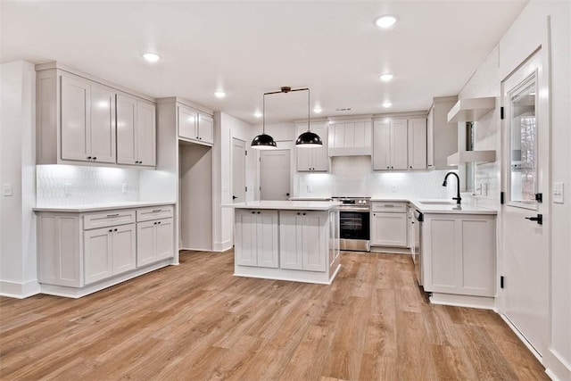 kitchen featuring wall chimney exhaust hood, appliances with stainless steel finishes, decorative light fixtures, light countertops, and a sink