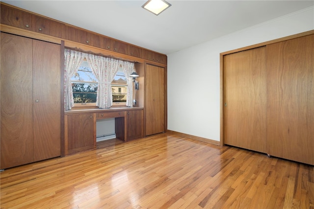 unfurnished bedroom featuring baseboards, built in study area, light wood-style flooring, a baseboard heating unit, and multiple closets