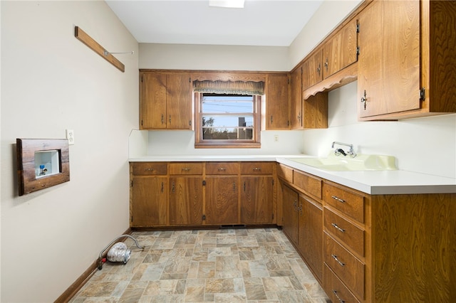 kitchen with baseboards, light countertops, stone finish flooring, and brown cabinets