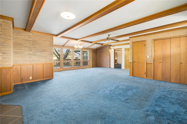 unfurnished living room featuring wooden walls, wainscoting, lofted ceiling with beams, carpet flooring, and ceiling fan with notable chandelier