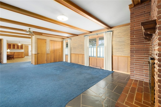 unfurnished living room with dark carpet, wood walls, wainscoting, and beam ceiling