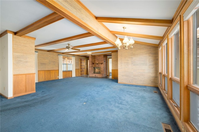 empty room with visible vents, vaulted ceiling with beams, dark colored carpet, a fireplace, and ceiling fan with notable chandelier