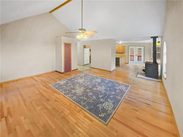 living area featuring high vaulted ceiling, light wood-type flooring, a wood stove, and ceiling fan