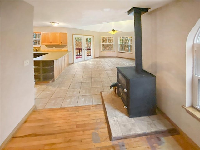 interior space featuring french doors, decorative light fixtures, light countertops, light brown cabinetry, and a wood stove