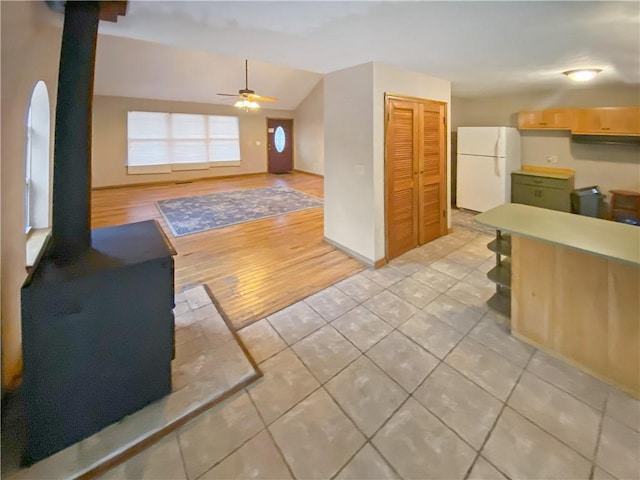 kitchen featuring open floor plan, freestanding refrigerator, a wood stove, vaulted ceiling, and light brown cabinetry