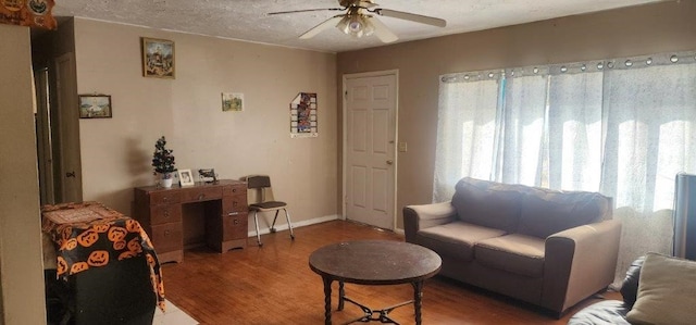 living room featuring ceiling fan, a textured ceiling, baseboards, and wood finished floors