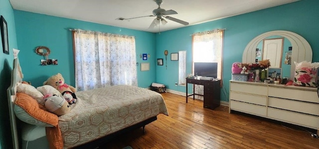 bedroom featuring a ceiling fan, wood finished floors, visible vents, and baseboards