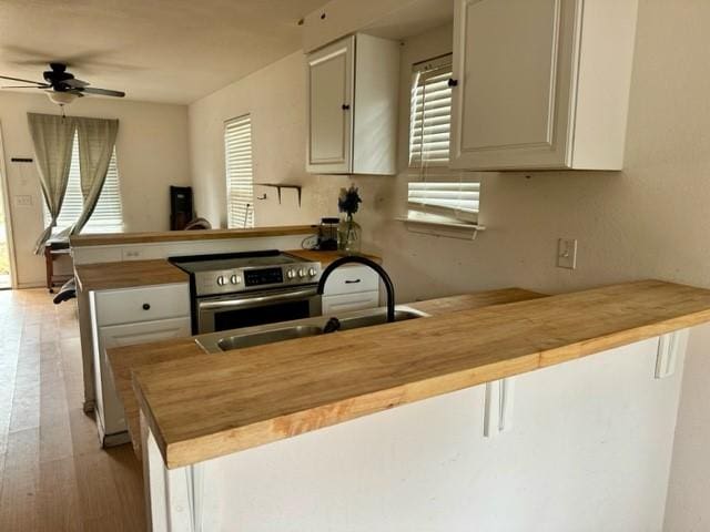 kitchen with a peninsula, a sink, wooden counters, light wood-type flooring, and stainless steel electric range