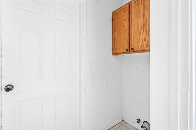 clothes washing area with light tile patterned flooring and cabinet space