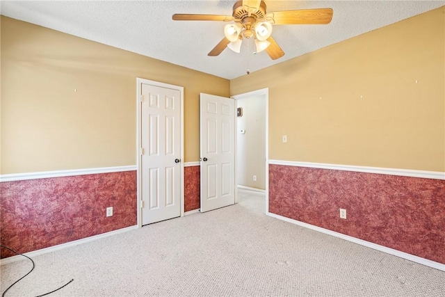 empty room featuring light carpet, ceiling fan, a textured ceiling, and wainscoting