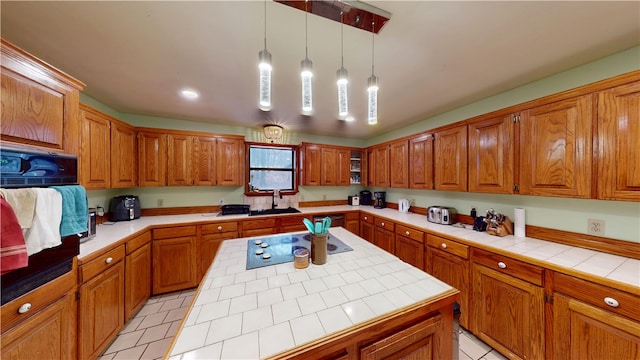 kitchen featuring black appliances, a sink, tile counters, and brown cabinets