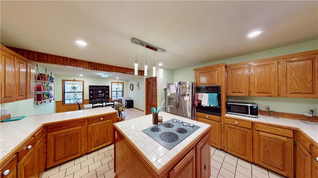 kitchen featuring tile counters, a center island, decorative light fixtures, and black appliances