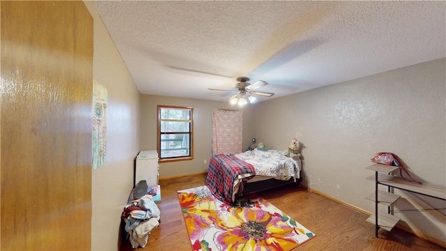 bedroom featuring a ceiling fan, a textured ceiling, baseboards, and wood finished floors