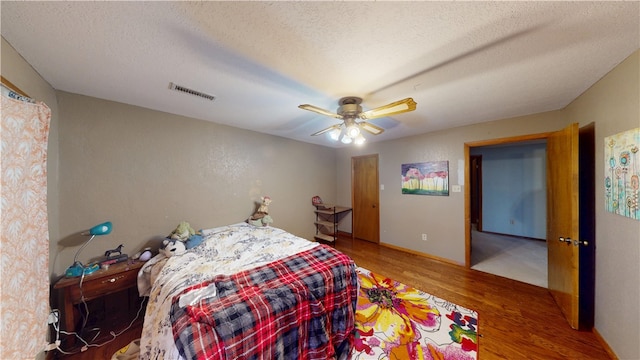 bedroom with a ceiling fan, a textured ceiling, visible vents, and wood finished floors