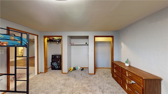 bedroom with light colored carpet, a textured ceiling, baseboards, and two closets