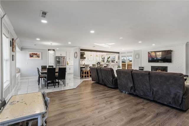 living room featuring light wood finished floors, ornamental molding, a brick fireplace, and visible vents