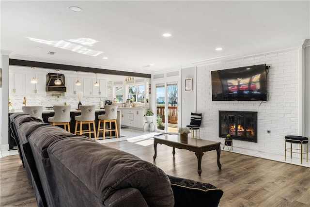 living area with a brick fireplace, crown molding, and wood finished floors