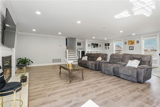 living area with visible vents, a glass covered fireplace, stairway, ornamental molding, and light wood-style floors