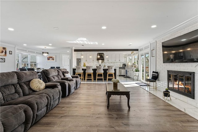 living room featuring light wood finished floors, ornamental molding, a fireplace, and recessed lighting