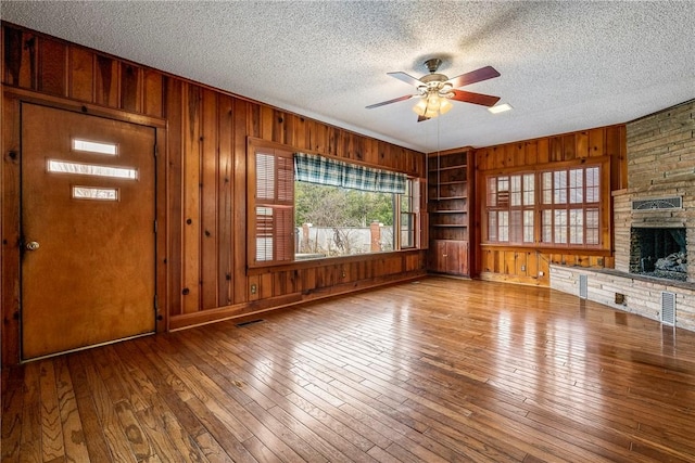510 W Central Ave, Bentonville, AR 72712 - unfurnished living room with a textured ceiling, a ceiling fan, wood finished floors, and a stone fireplace