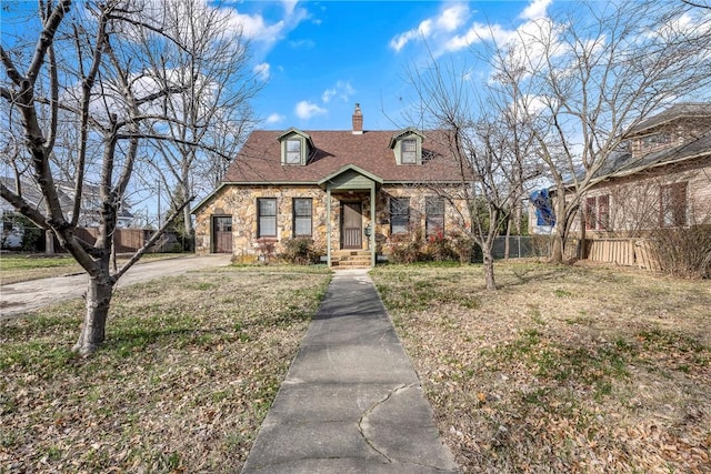 view of front of home with driveway, stone siding, fence, and a chimney