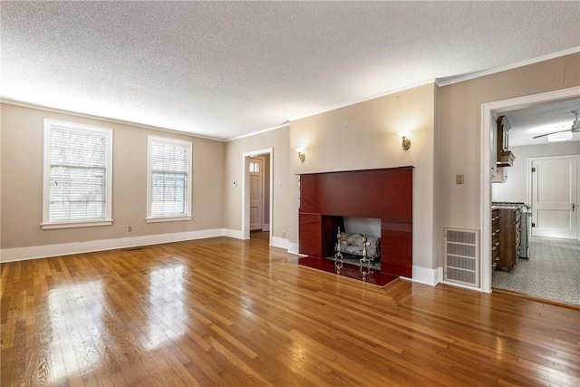 unfurnished living room featuring ornamental molding, visible vents, a textured ceiling, and wood finished floors