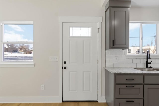 kitchen featuring a wealth of natural light, light stone counters, backsplash, and a sink