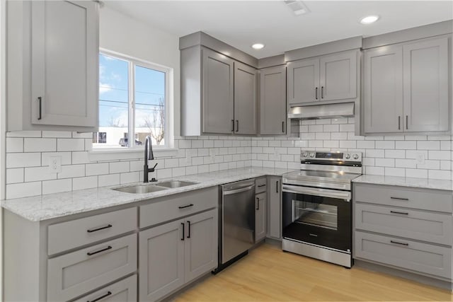 kitchen with light stone countertops, gray cabinets, stainless steel appliances, under cabinet range hood, and a sink