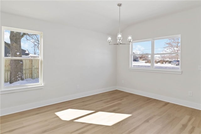 spare room with a notable chandelier, wood finished floors, a wealth of natural light, and baseboards