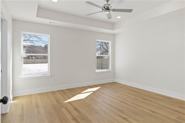 unfurnished room featuring light wood finished floors, a raised ceiling, and baseboards