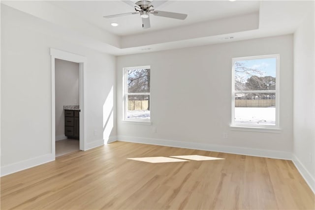 unfurnished room featuring a tray ceiling, light wood-type flooring, and baseboards