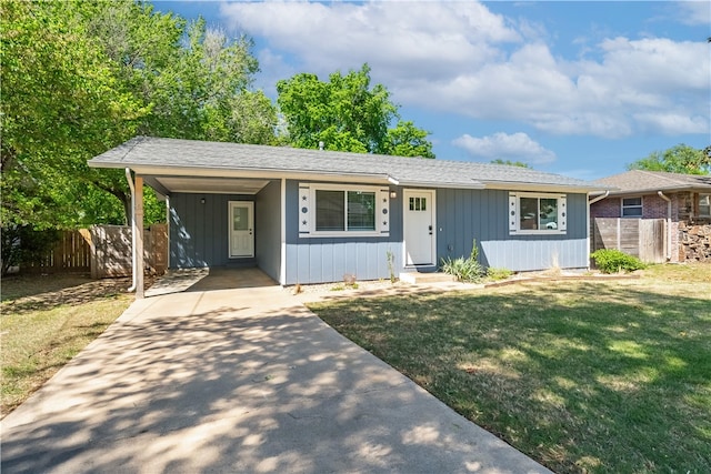 view of front facade featuring driveway, an attached carport, a front yard, and fence