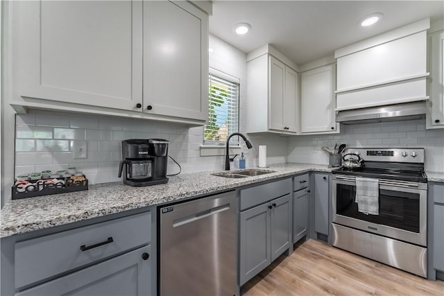 kitchen with gray cabinetry, exhaust hood, a sink, appliances with stainless steel finishes, and light wood-type flooring