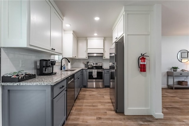 kitchen featuring stainless steel appliances, light wood-type flooring, a sink, and gray cabinetry