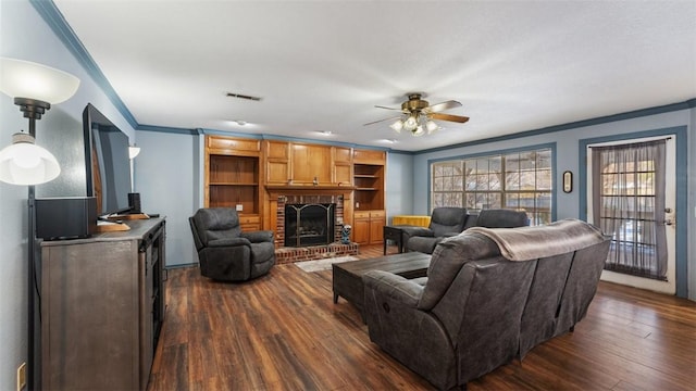 living room featuring visible vents, a ceiling fan, ornamental molding, a brick fireplace, and dark wood-style floors