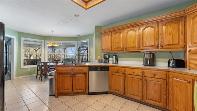 kitchen featuring a sink, light countertops, stainless steel dishwasher, hanging light fixtures, and brown cabinetry