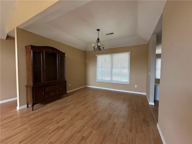 unfurnished dining area featuring a chandelier, a raised ceiling, visible vents, and wood finished floors