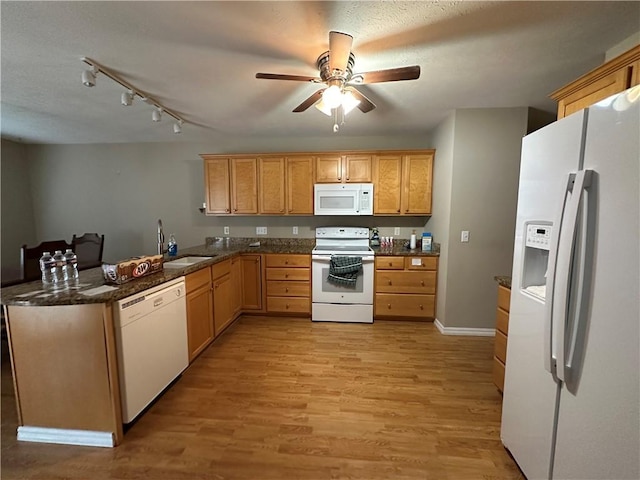 kitchen with light wood-style flooring, a sink, dark stone counters, white appliances, and a peninsula