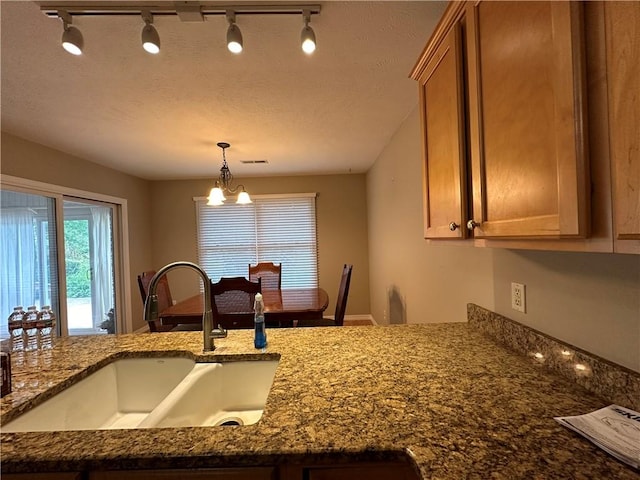 kitchen with brown cabinetry, dark stone countertops, decorative light fixtures, a chandelier, and a sink