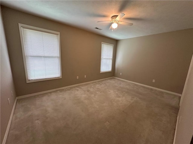 carpeted spare room with baseboards, visible vents, and a ceiling fan