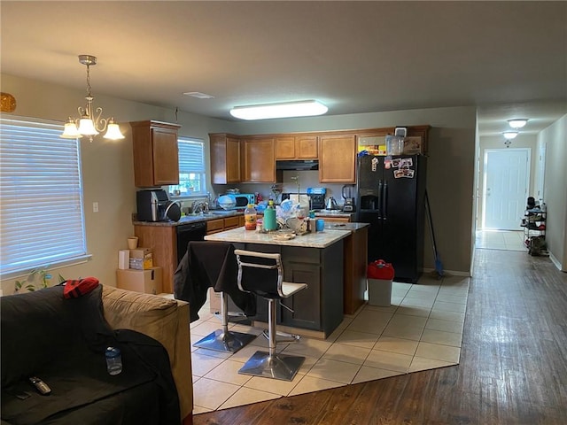 kitchen with a kitchen island, light wood-style flooring, black appliances, decorative light fixtures, and exhaust hood